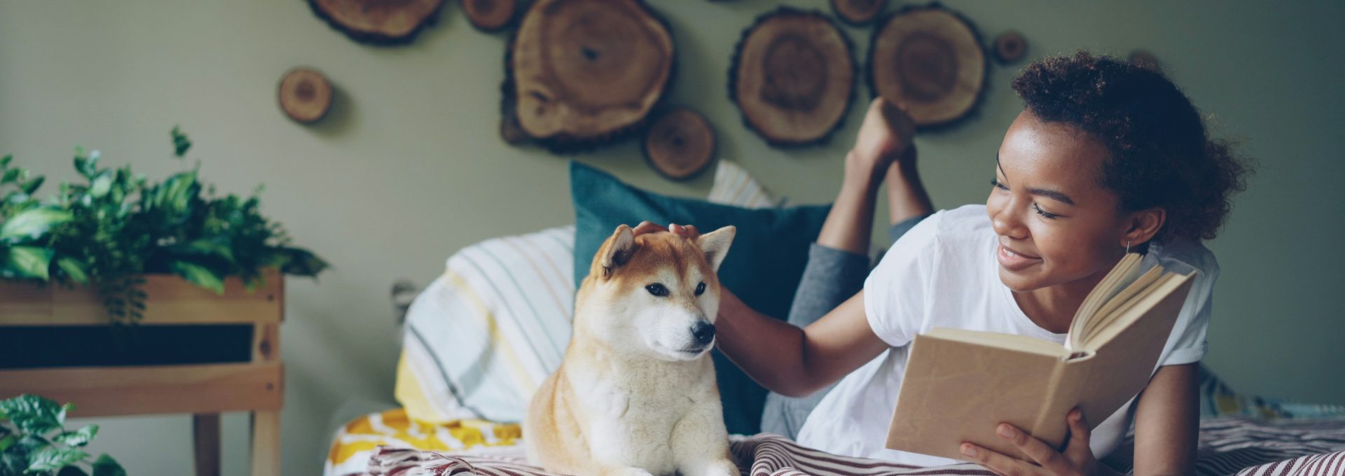 Girl pets a dog while reading in bed.